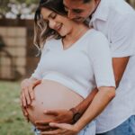 Two people standing outdoors. One is pregnant and the other has their arms around the pregnant individual.